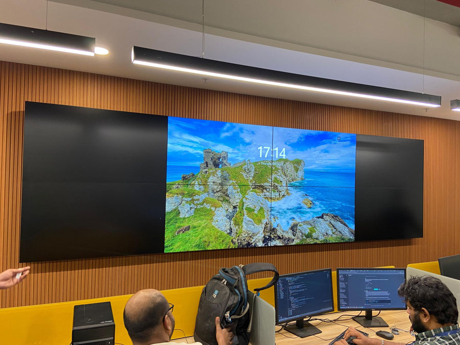 Four-panel large-format video wall installed in a command centre style facility in India, integrated with adjacent operator workstations for real-time monitoring